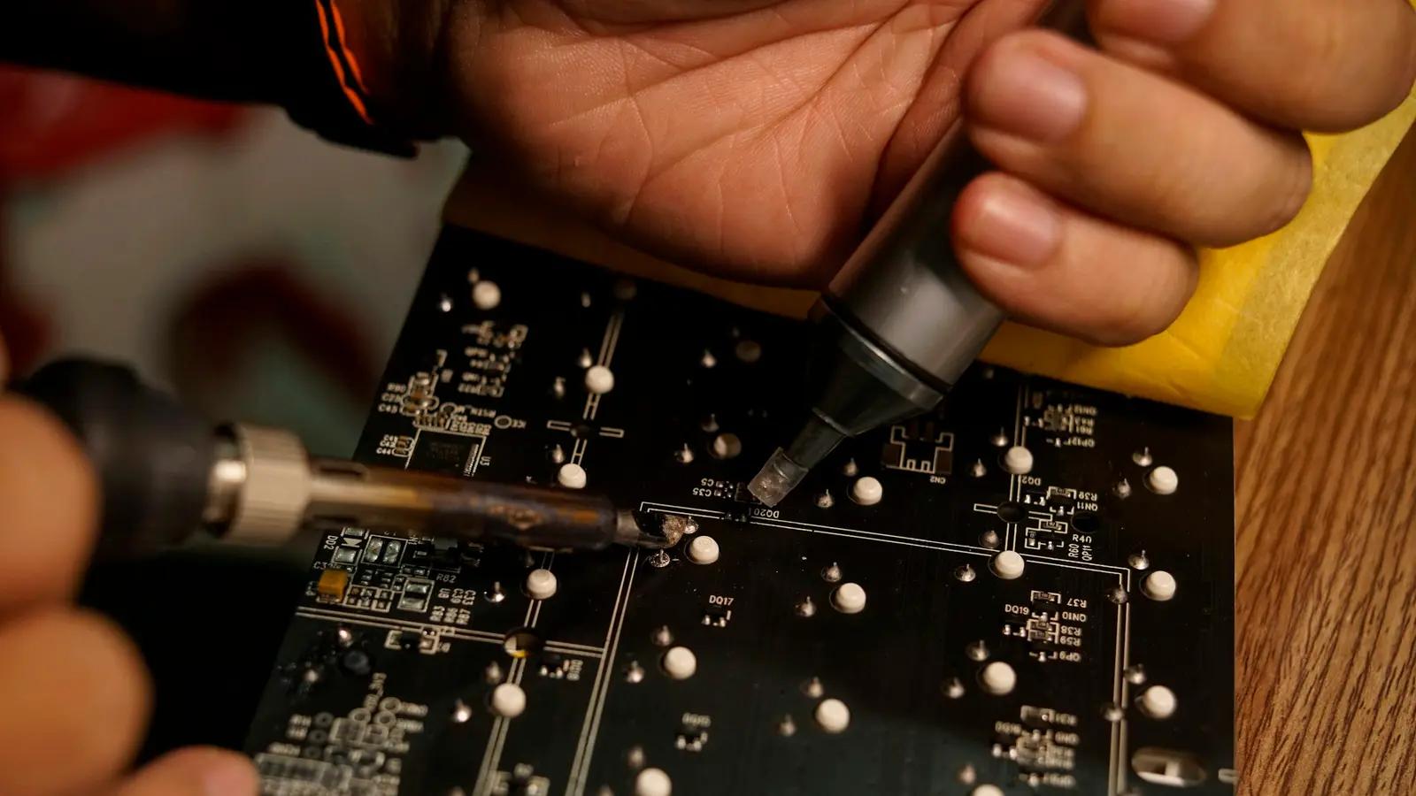 Hands soldering components on a dark circuit board